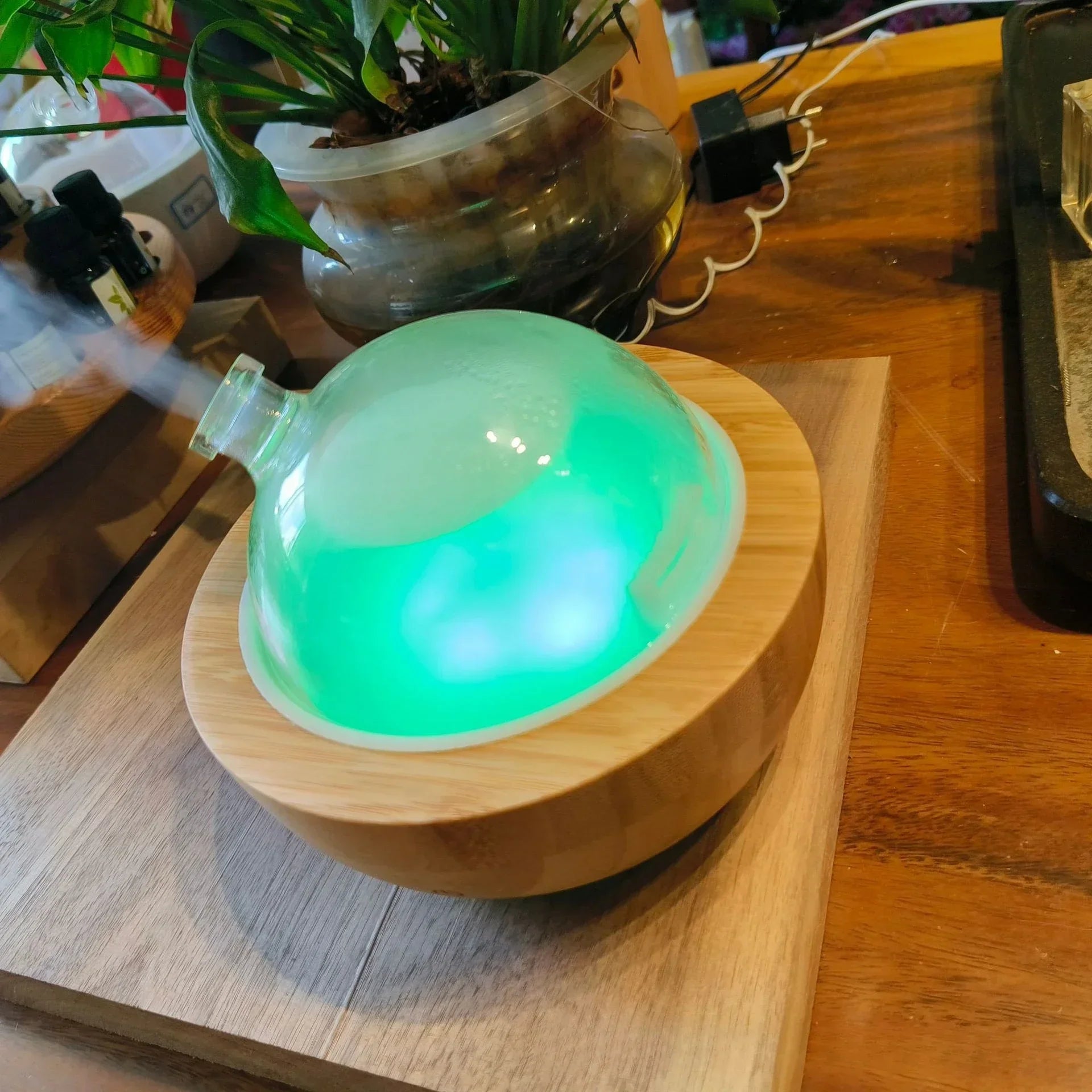 SereneGlow Glass Aromatherapy diffuser with glass dome and wood base emitting green LED light on wooden surface